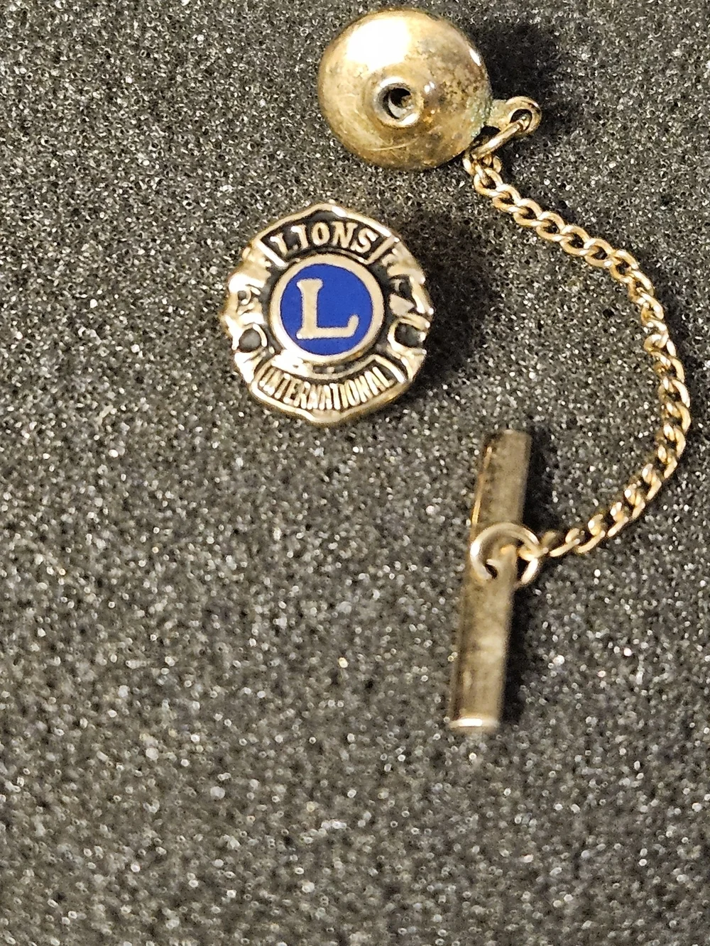 A vintage gold-tone Lions Club International tie tack and lapel pin with a chain
